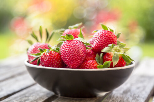 Bowl of strawberries on wooden garden table - SARF002705