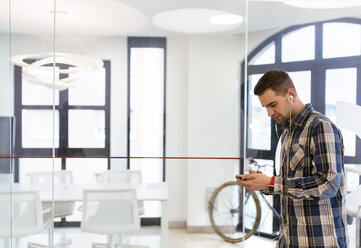 Junger Mann mit Ohrstöpseln im Büro - MGOF001769