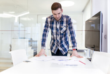 Junger Mann am Schreibtisch im Büro, der Dokumente betrachtet - MGOF001772