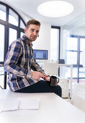 Junger Mann mit einer Tasse Kaffee und einem Bluetooth-Headset im Büro - MGOF001777