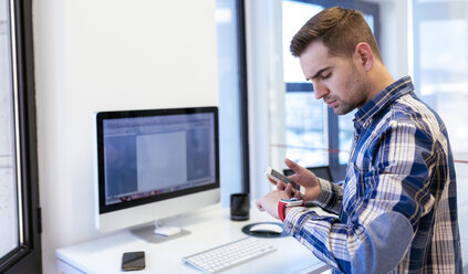 Young man with cell phone and smartwatch in office - MGOF001783