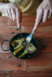 Hände einer Frau, die auf dem Grill zubereitete Artischocken isst, Nahaufnahme - KIJF000366