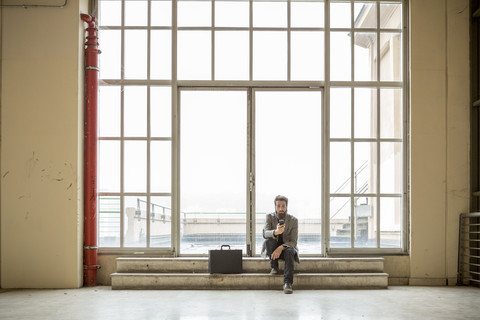 Hipster-Geschäftsmann mit Aktentasche wartet vor einer Tür in einem Industriegebäude, lizenzfreies Stockfoto