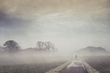 Gernany, North Rhine-Westphalia, Silhouette of a man standing on foggy country road - DWIF000735