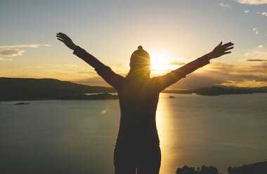 Peru, Amantani Island, silhouette of woman with raised arms enjoying sunset from Pachamama peak - GEMF000878