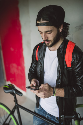 Junger Mann mit Fahrrad schaut auf Smartphone, lizenzfreies Stockfoto