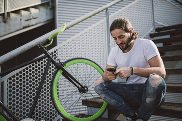 Young man sitting on stairs looking at smartphone - RAEF001119