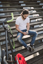 Junger Mann sitzt auf einer Treppe und schaut auf sein Smartphone - RAEF001123