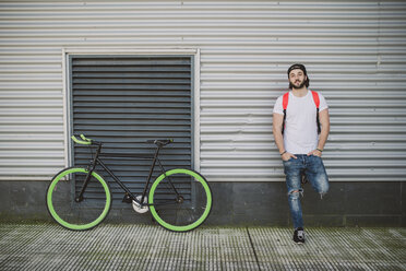 Junger Mann lehnt neben einem Fixie-Fahrrad an der Wand - RAEF001129