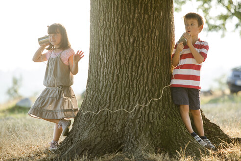 Kleiner Junge und Mädchen spielen mit Blechdose Telefon in der Natur - ZOCF000115