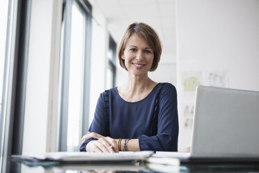 Portrait of smiling businesswoman at office desk - RBF004415
