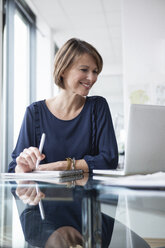 Lächelnde Geschäftsfrau arbeitet am Laptop im Büro - RBF004417