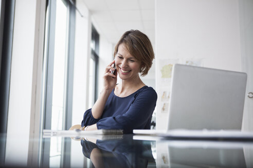 Lächelnde Geschäftsfrau am Mobiltelefon im Büro - RBF004418