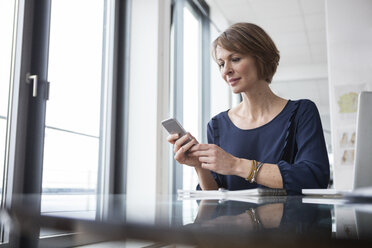 Geschäftsfrau schaut auf Handy am Schreibtisch - RBF004419