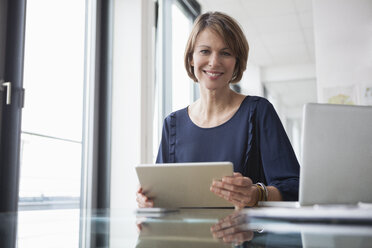 Porträt einer lächelnden Geschäftsfrau mit digitalem Tablet am Bürotisch - RBF004420
