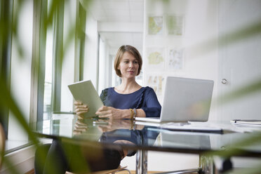 Businesswoman with digital tablet and laptop at office desk - RBF004421