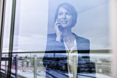 Businesswoman on cell phone behind windowpane - RBF004439