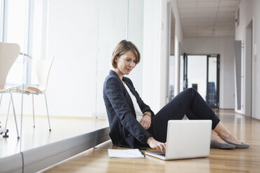 Businesswoman sitting on office floor using laptop - RBF004449