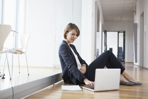 Geschäftsfrau sitzt auf dem Büroboden und benutzt einen Laptop - RBF004449