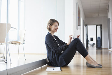 Businesswoman sitting on office floor using digital tablet - RBF004450