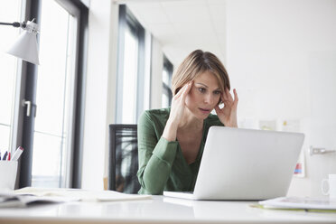 Concentrated businesswoman working on laptop at office desk - RBF004463