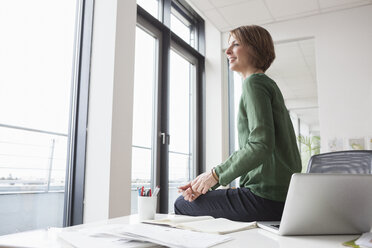 Geschäftsfrau auf Bürotisch mit Blick aus dem Fenster - RBF004465