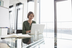 Lächelnde Geschäftsfrau arbeitet am Laptop im Büro - RBF004469