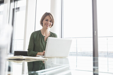 Porträt einer lächelnden Geschäftsfrau, die an einem Laptop im Büro arbeitet - RBF004471