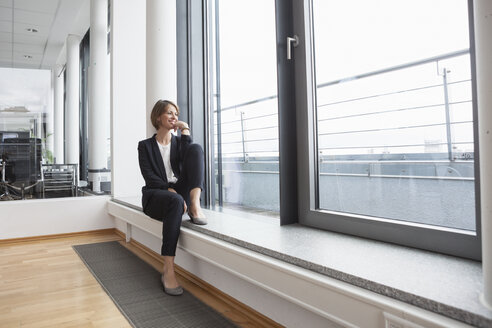 Lächelnde Geschäftsfrau auf der Fensterbank sitzend - RBF004475