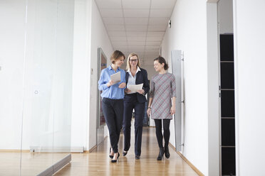 Three businesswomen walking and talking in office hall - RBF004498