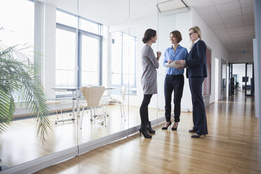 Drei Geschäftsfrauen diskutieren in einer Bürohalle - RBF004499