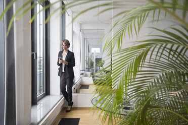 Businesswoman looking on cell phone at office window - RBF004528