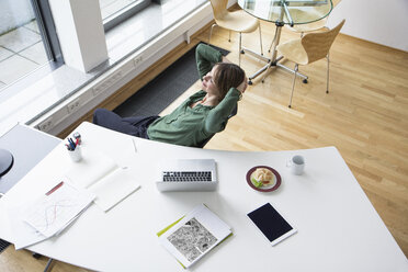 Lächelnde Geschäftsfrau am Bürotisch lehnt sich zurück - RBF004529