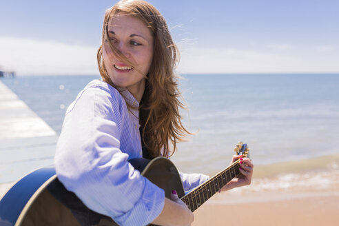 Lächelnde junge Frau mit Gitarre am Meer - BOYF000287