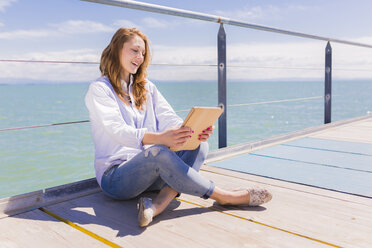 Porträt einer jungen Frau, die ein digitales Tablet vor dem Meer benutzt - BOYF000298