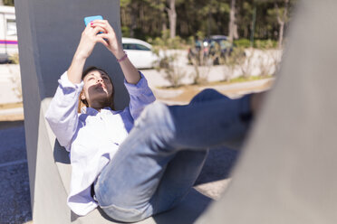 Italien, eine Frau macht ein Selfie mit ihrem Smartphone, während sie sich im Schatten ausruht - BOYF000302