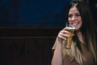 Smiling woman drinking a glass of beer in a bar - ABZF000386