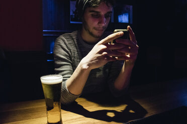 Mann benutzt sein Telefon an einer Theke mit einem Glas Bier - ABZF000394