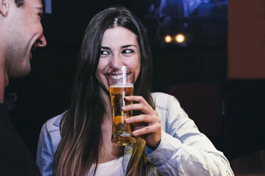 Smiling woman drinking a glass of beer with a man in a bar - ABZF000397