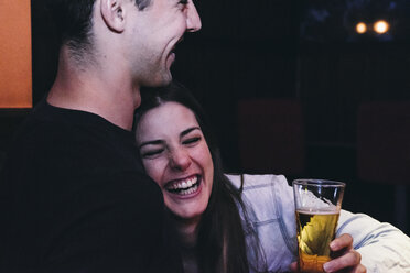 Laughing woman leaning on the chest of a man drinking beer in a bar - ABZF000398