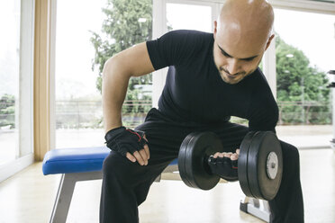 Man lifting a dumbbell sitting on a bench in a gym - ABZF000407