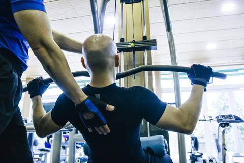 Mann bei Brustübungen in einem Fitnessstudio, unterstützt von seinem Trainer, lizenzfreies Stockfoto