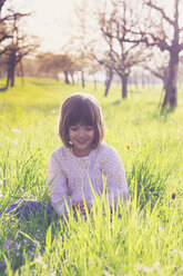 Porträt eines lächelnden kleinen Mädchens, das auf einer Wiese im Frühling sitzt - LVF004827