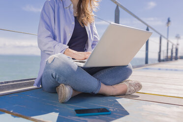 Junge Frau mit Laptop und Smartphone, auf dem Steg sitzend - BOYF000325