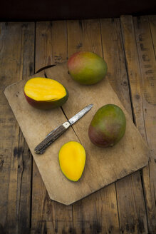 Ganze und in Scheiben geschnittene Mango und Taschenmesser auf Holzbrett - LVF004834