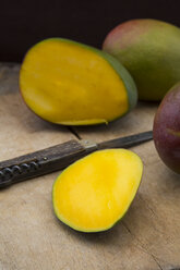 Whole and sliced mango and pocket knife on wood - LVF004835