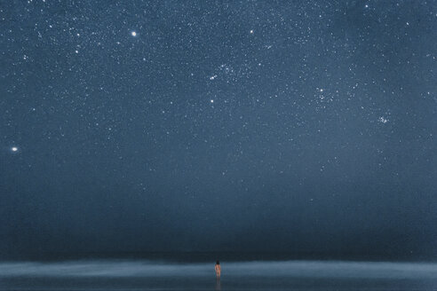 Rear view of nude man standing in water, looking to stars at night - WV000758
