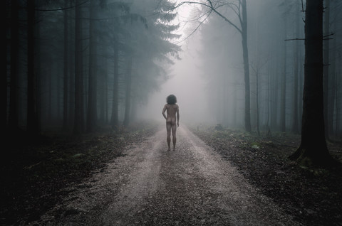 Rückansicht eines nackten Mannes auf einem Weg im nebligen Wald, lizenzfreies Stockfoto