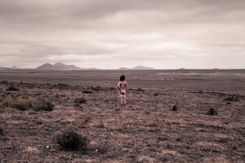 Lanzarote, Caleta de Famara, Rear view of nude man standing in bleak landscape - WV000771