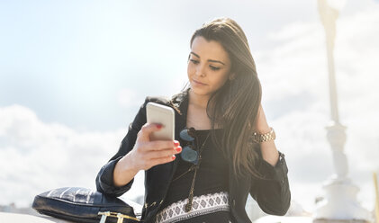 Junge schöne Frau sendet eine Nachricht mit dem Smartphone am Strand - MGOF001811